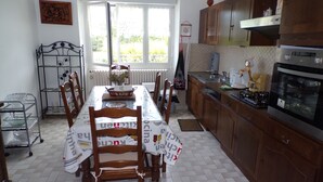 A dining area with a table set for four, surrounded by wooden chairs. A kitchen with wooden cabinets and a stove is adjacent to the dining area. - House of Lacaze 2 ears (Toulonjac)