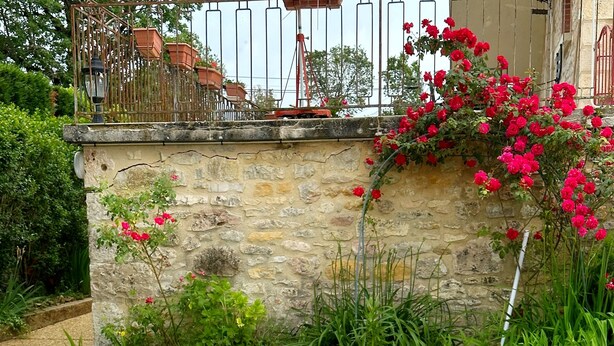 A garden with a stone wall, metal fence, and a table with a decorative metal fence in the foreground. - House of Lacaze 2 ears (Toulonjac)