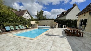 Un patio trasero con piscina, sillas de descanso y una mesa de picnic.