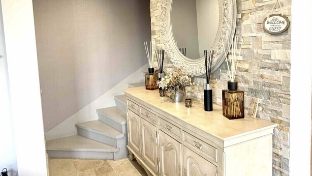Una escalera con un muro color crema y un muro de piedra, un espejo y elementos decorativos.