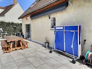 A patio with a wooden table and benches, a blue folding screen, and a wall-mounted heater.