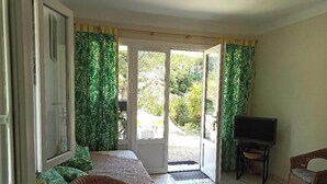 A room with a bed, a television on a stand, and a door leading to an outdoor area with greenery. - T2 ground floor Carry le Rouet (Carry-Le-Rouet)