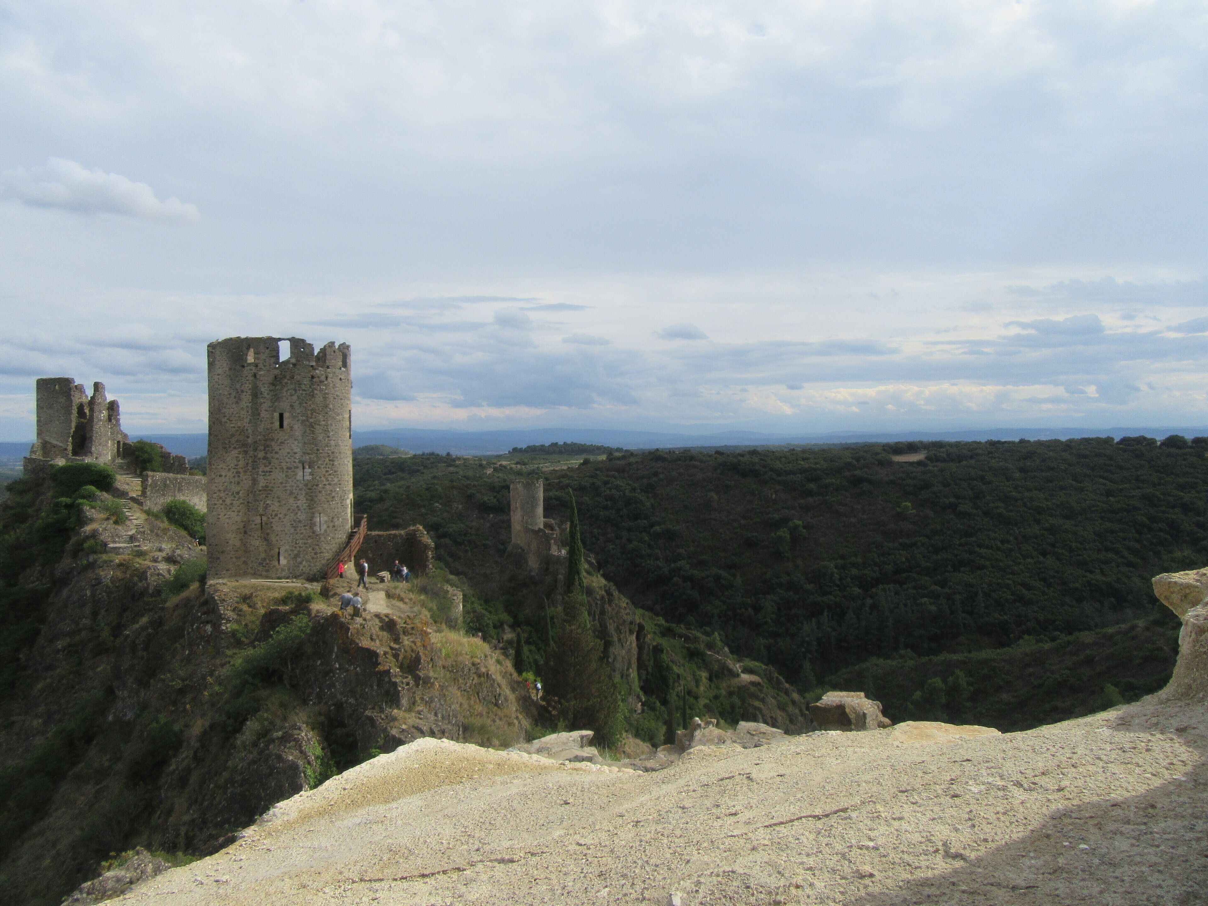 A historical stone castle on a hill with ruins and a forested landscape in the background.
