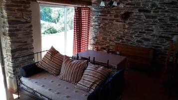 A stone-walled room with a bed, a window with curtains, and a chandelier.