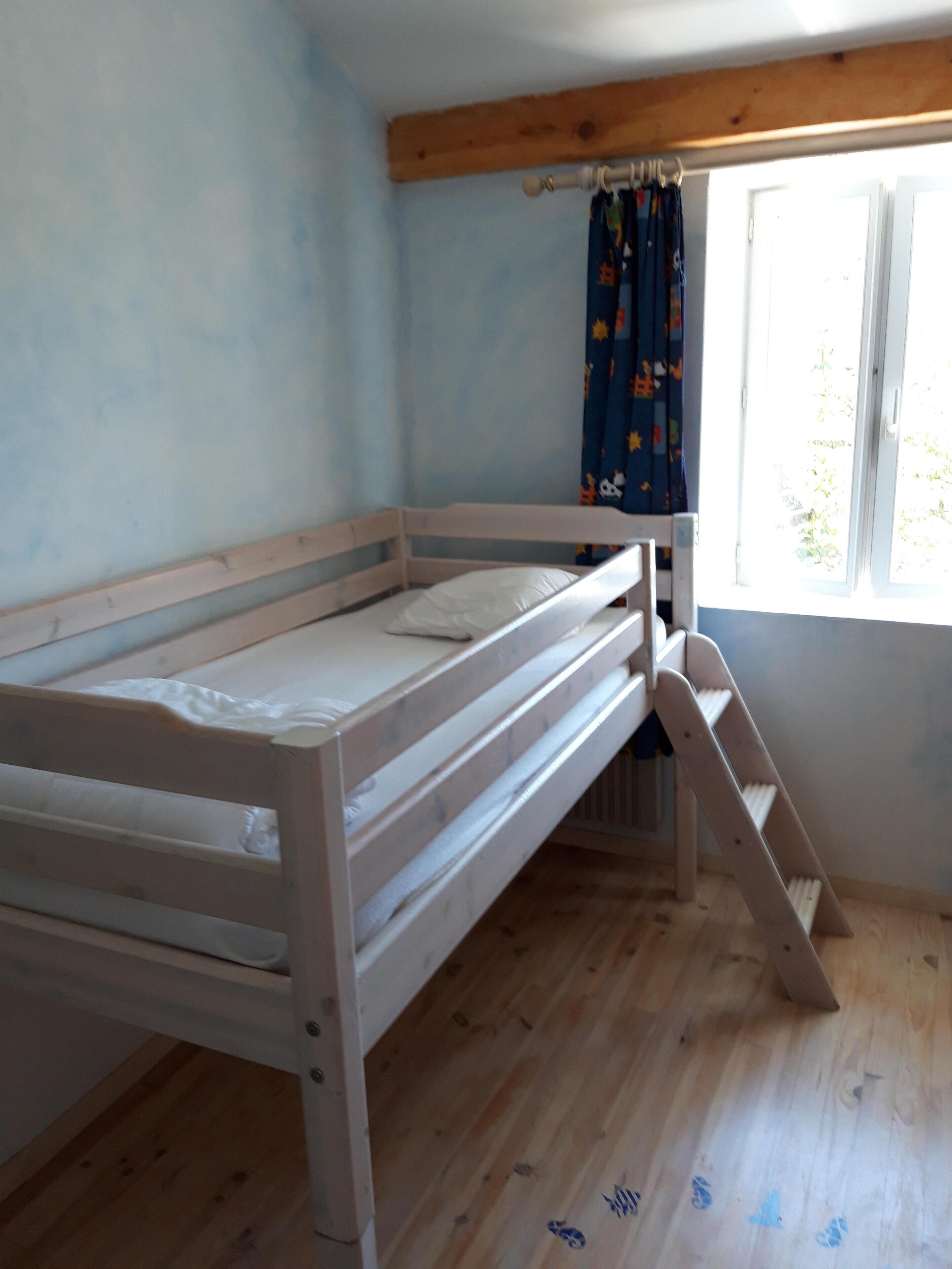A single wooden bunk bed with a small ladder, a window with curtains, and a wooden floor.