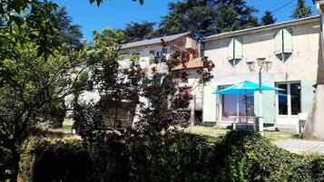 Un edificio de dos pisos con un balcón, una sombrilla azul y un muro de piedra al frente.