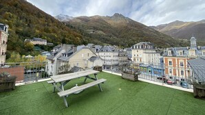A residential area with a green lawn, picnic table, and buildings with varied architecture. - Place de la mairie T2 type loft 70m2 terrasse 35m2 (Cauterets)