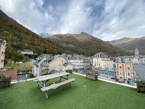 Blick auf eine Stadt mit Gebäuden, einem Picknicktisch und Bergen im Hintergrund.