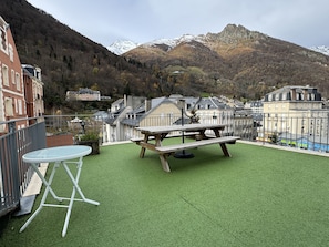 Une terrasse sur le toit, avec une table et des chaises en bois, d’où l’on peut admirer un paysage montagneux et une ville située en contrebas.