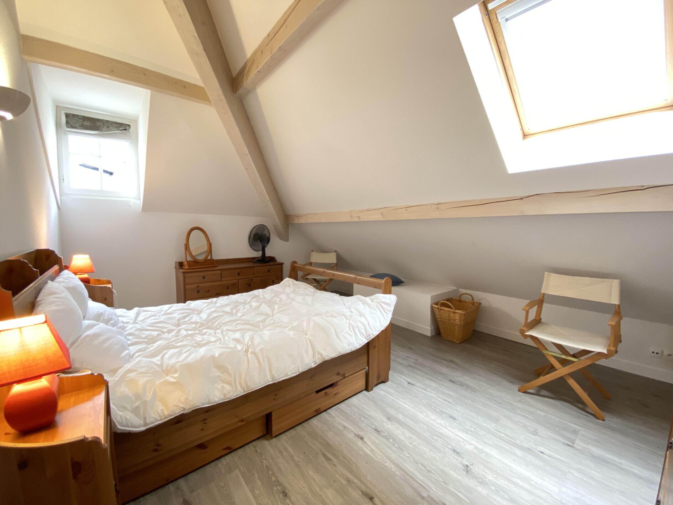A bedroom with a wooden bed, a dresser, a chair, a window, and a fan.