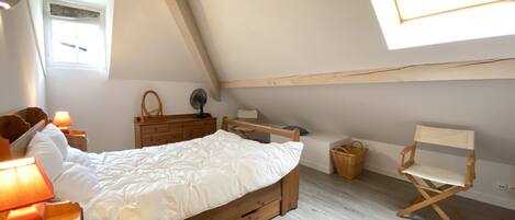 A bedroom with a wooden bed, a dresser, a chair, a window, and a fan.