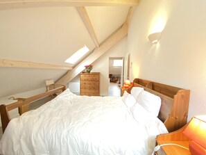 A bedroom with a sloped ceiling, a wooden bed, a dresser, and a nightstand with a lamp.