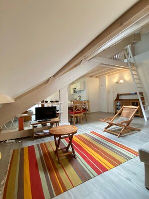 Un dormitorio estilo loft con televisor, muebles de madera, un tapete a rayas y una escalera que lleva a un nivel superior.