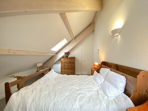 A bedroom with a sloped ceiling, a wooden bed, a nightstand with a lamp, a dresser, and a skylight. - Place de la mairie T2 type loft 70m2 terrasse 35m2 (Cauterets)