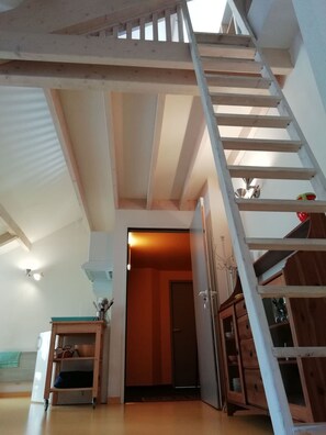 Un escalier en bois menant à un niveau supérieur, un coin cuisine avec des placards et une porte donnant sur une autre pièce.