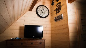 Une pièce aux murs lambrés, avec une horloge, un téléviseur à écran plat posé sur un meuble en bois et une porte.