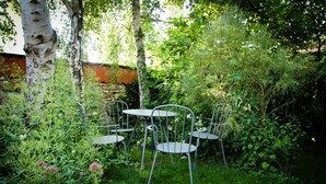 Un jardin avec un mur en pierre, des chaises en métal et une table.