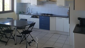 A compact kitchen with a gas stove, white cabinets, and a dining area with a table and chairs. - Guirec Dogs (Perros-Guirec)
