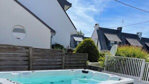 A rectangular hot tub with a grey exterior and a white interior, surrounded by a wooden fence and grass. - Guirec Dogs (Perros-Guirec)