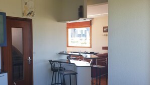 A compact kitchen with a dining area, a wooden door, and a small bar stool. - Guirec Dogs (Perros-Guirec)