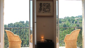 Un balcon avec des fauteuils en osier, une applique murale et un tableau encadré.