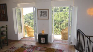 Une pièce avec vue sur une forêt, des fauteuils en osier, un tapis et un tableau encadré au mur.