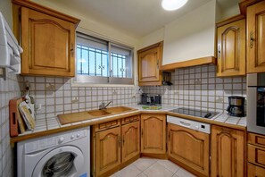 A compact kitchen with wooden cabinets, a built-in washing machine, and a coffee maker.
