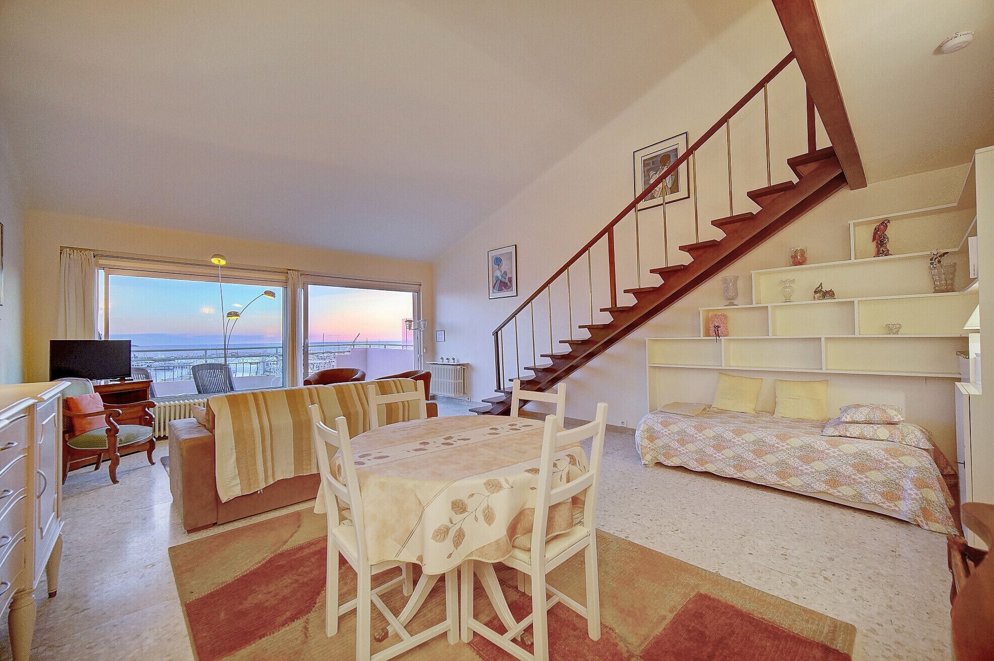 Una sala de estar con comedor, escalera y cama.