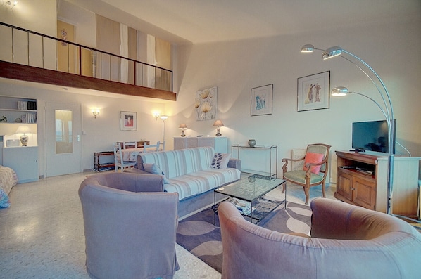Un salón espacioso con techo alto, una escalera, un televisor y un comedor.