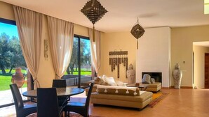 A spacious living room with a large window, a sofa set, a dining table with chairs, and a decorative hanging light fixture. - Villa Kristy Junior (2 bedrooms + Private pool) (Marrakesh)