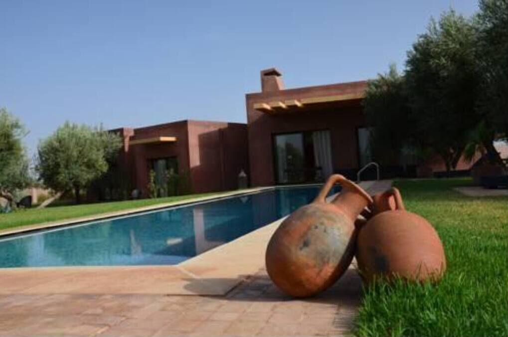 Une maison moderne avec une piscine et un grand pot rouillé posé sur la pelouse.