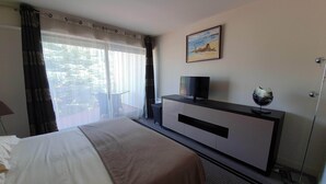 Ein Hotelzimmer mit Bett, Fernseher auf einem Schrank, einem Bild an der Wand und einem Fenster mit Vorhängen.