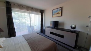 A hotel room with a bed, a TV on a cabinet, a painting on the wall, and a window with curtains.