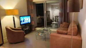 Ein Wohnzimmer mit Fernseher, einem Glastisch, einer Couch und einer Lampe.