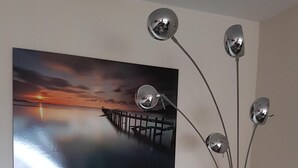 Ein modernes Badezimmer mit einem Glaswaschtisch, einem großen Spiegel und einem Gemälde, das einen Sonnenuntergang über einem Steg zeigt.