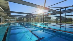 Ein Schwimmbecken mit klarem, blauem Wasser, umgeben von großen Fenstern und einer Metallkonstruktion als Dach.