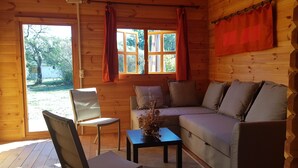 Ein gemütliches Blockhaushaus-Interieur mit Holzvertäfelung, einer Couch, einem Sessel, einem kleinen Tisch und einem Fenster mit Vorhängen.