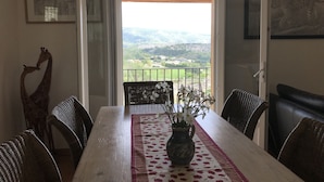 A dining area with a table set for four, a vase of flowers, and a view of the countryside through an open door. - La Casa, Charming little house of Provence  (Ongles)
