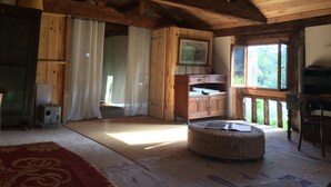 A rustic wooden room with a high ceiling, a wicker ottoman, a wooden cabinet, and a window with a view of greenery. - 100 years old  BARN revovated (Castets)