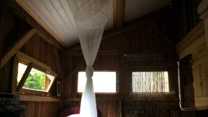A wooden cabin room with a bed, a small table, and a chair. There are windows with curtains and a mosquito net above the bed. - 100 years old  BARN revovated (Castets)