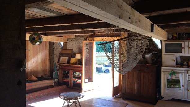 A rustic wooden interior with a wooden ceiling, a small round table, a hammock, and a cabinet with various items. - 100 years old  BARN revovated (Castets)