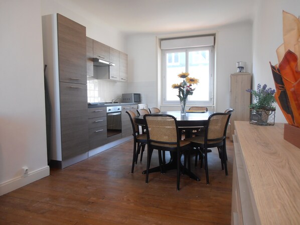 A modern kitchen with built-in appliances, a dining area with a wooden table and chairs, and a large window with a view.