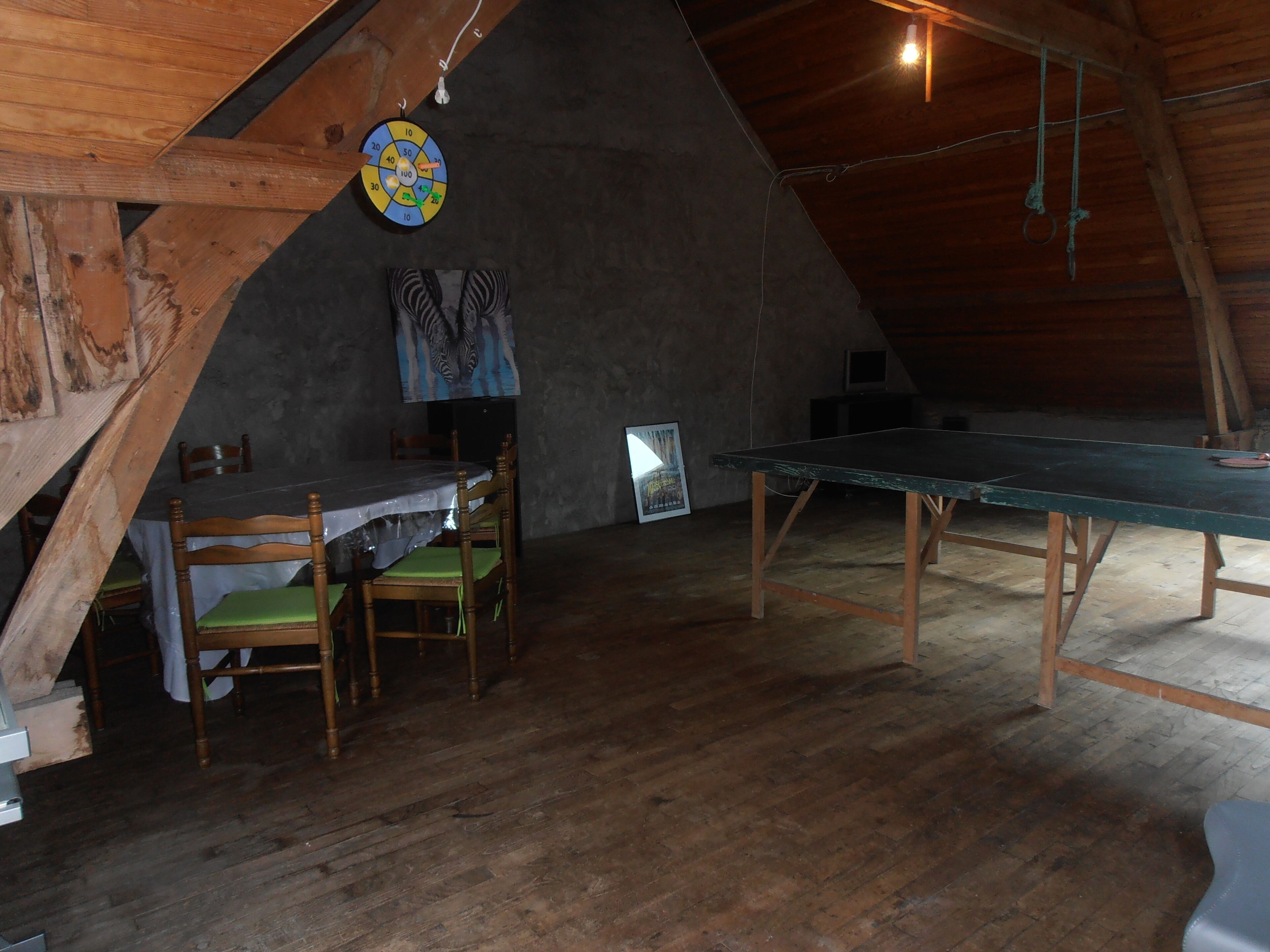 Ein rustikales Dachzimmer mit Holztisch, Stühlen und Dartscheibe.