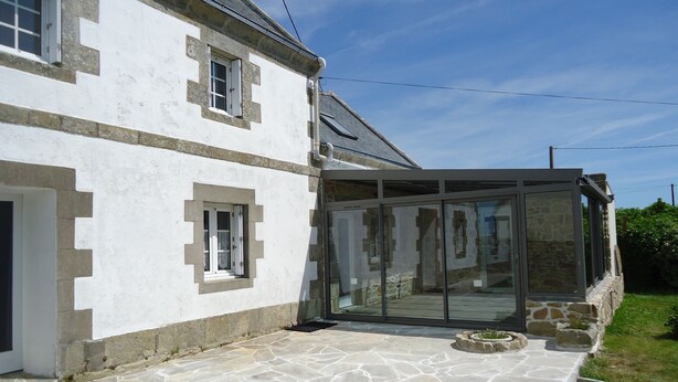 A house with a stone patio, a glass-enclosed porch, and a white exterior.