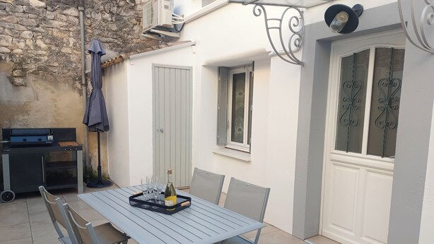 An outdoor patio with a table, chairs, a grill, and a bottle of wine.