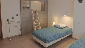 A bedroom with a bunk bed, a ladder, a metal drying rack, a bedside lamp, and a wall-mounted mirror.