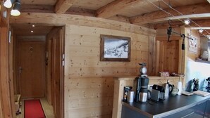 Et interiør af en træhytte med et tekøkken, der indeholder kaffemaskine, elkedel og redskaber.