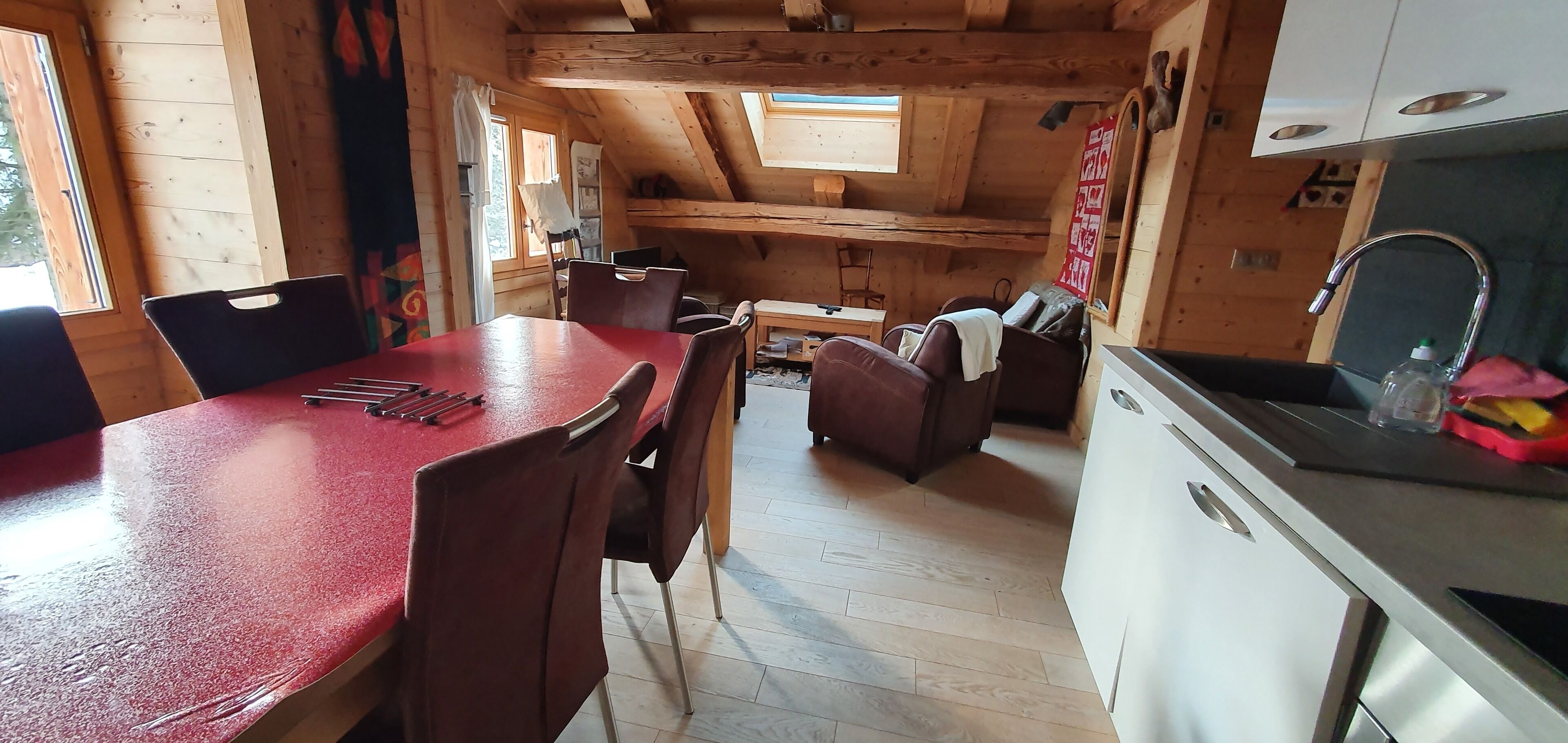 Een compacte keuken met houten wanden, een eethoek met rode stoelen, en een kleine keukenunit.