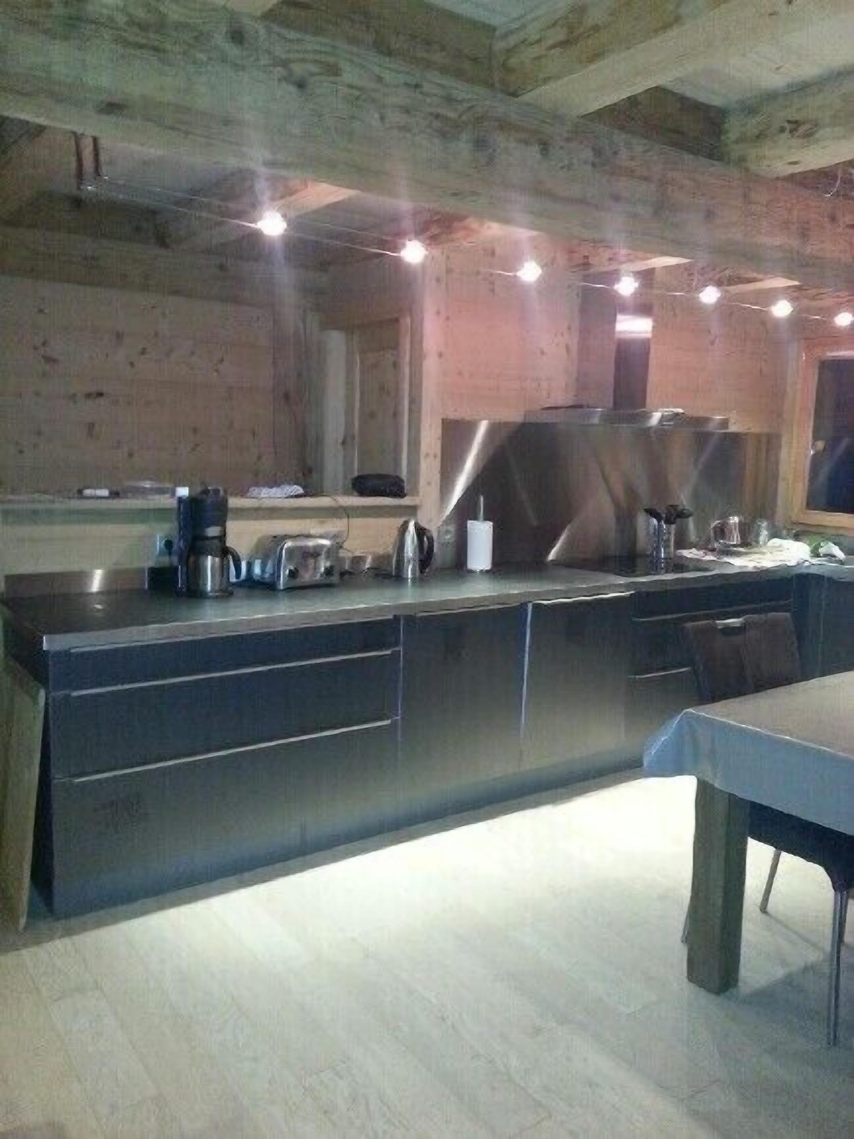 Een moderne keuken met roestvrijstalen apparatuur, houten balken in het plafond en een centraal eiland met een spoelbak en aanrecht.