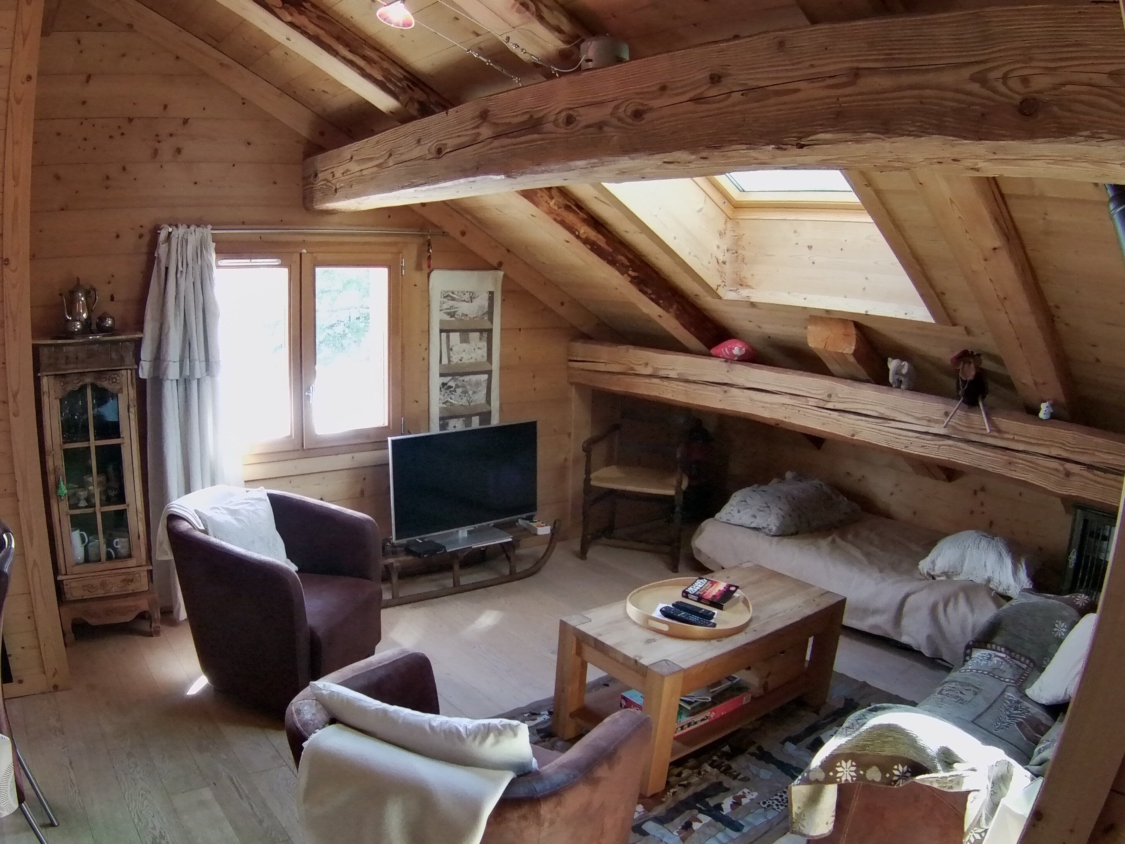 Une pièce mansardée chaleureuse avec un plafond en bois, une télévision, un canapé et un fauteuil.